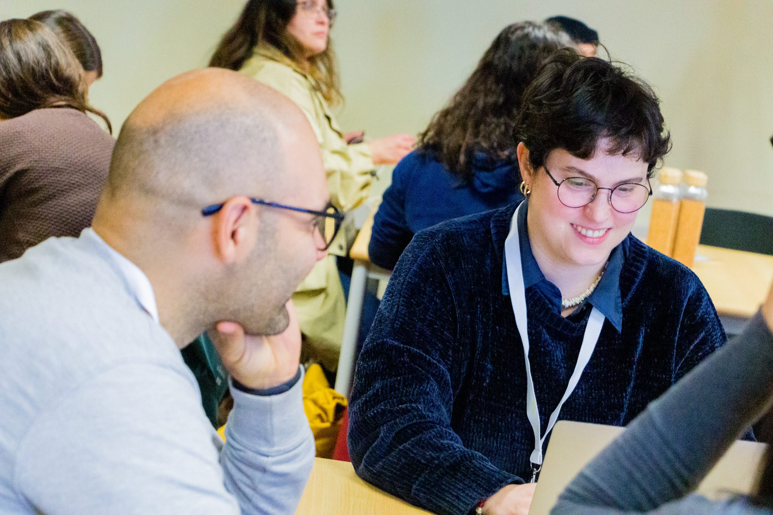 Dois participantes trocam ideias no workshop, com expressões sorridentes, enquanto utilizam um computador portátil