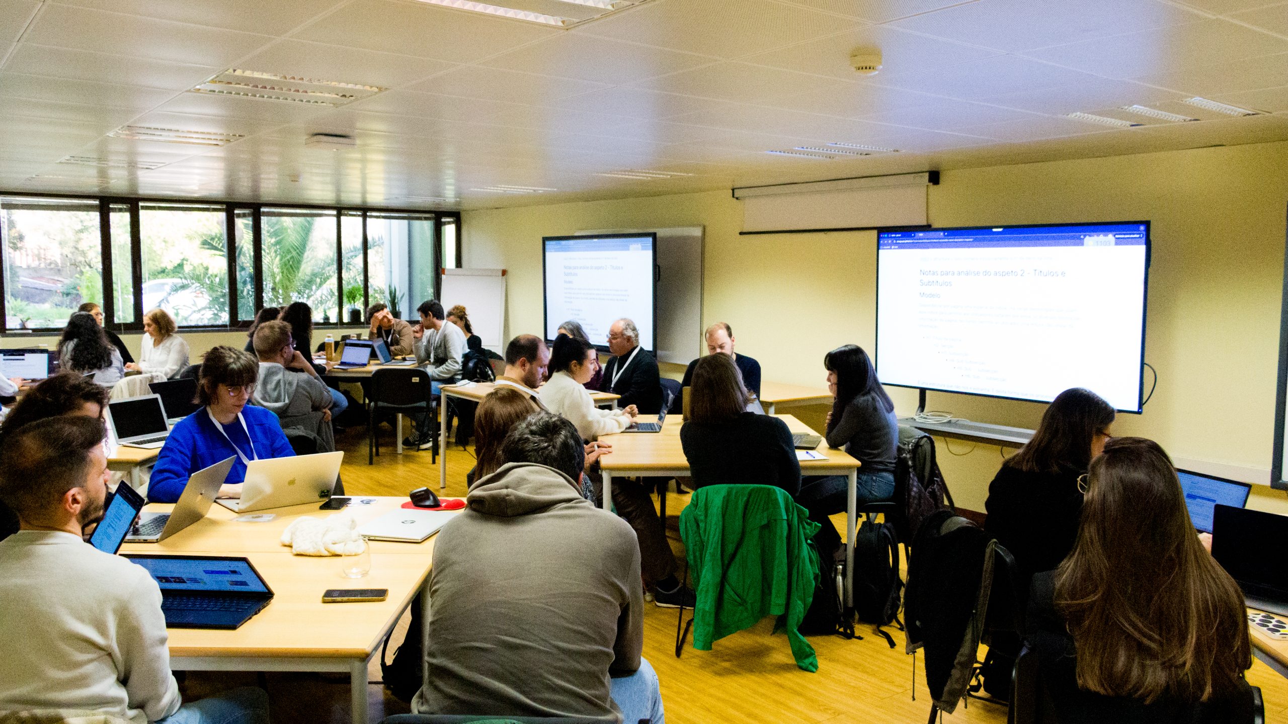 Sala cheia de participantes em vários grupos de trabalho durante um workshop das Jornadas